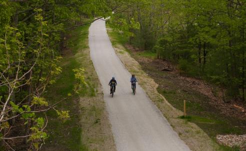 A pair of bicyclists on the rail trail in a green wood